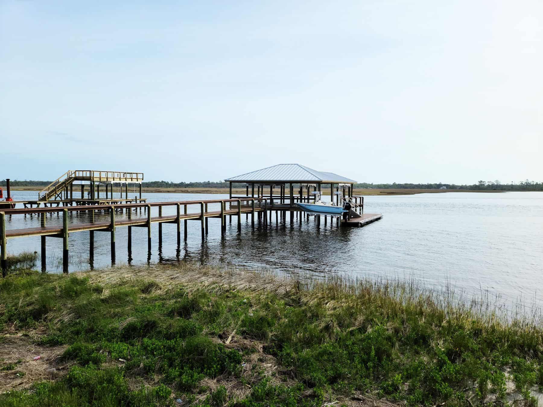 Long timber dock running out across marsh grass to a covered dock at the end