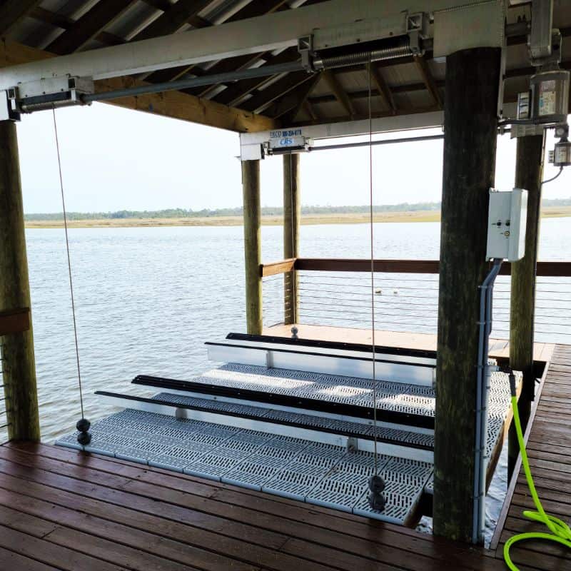 Empty aluminum boat lift with grated bunks lowered under a covered dock beside a marsh