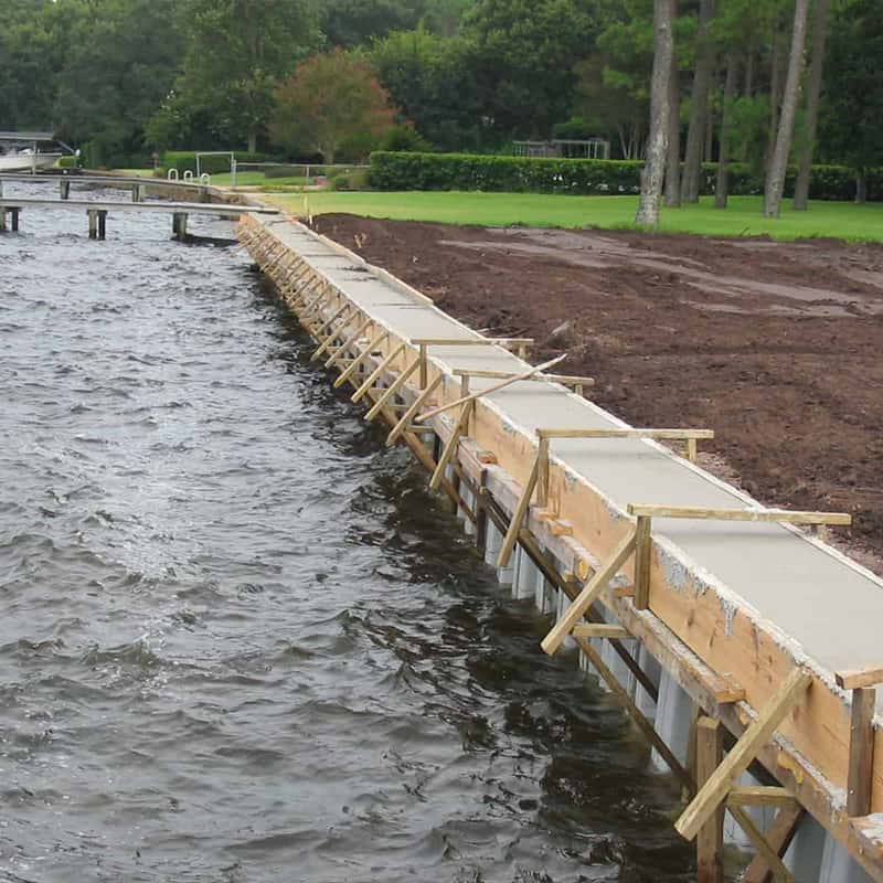 Seawall under construction with concrete cap forms and wood bracing along a windy lakefront