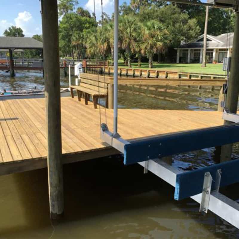 Boat lift with blue bunk beams and cables alongside a fresh wood dock deck and bench