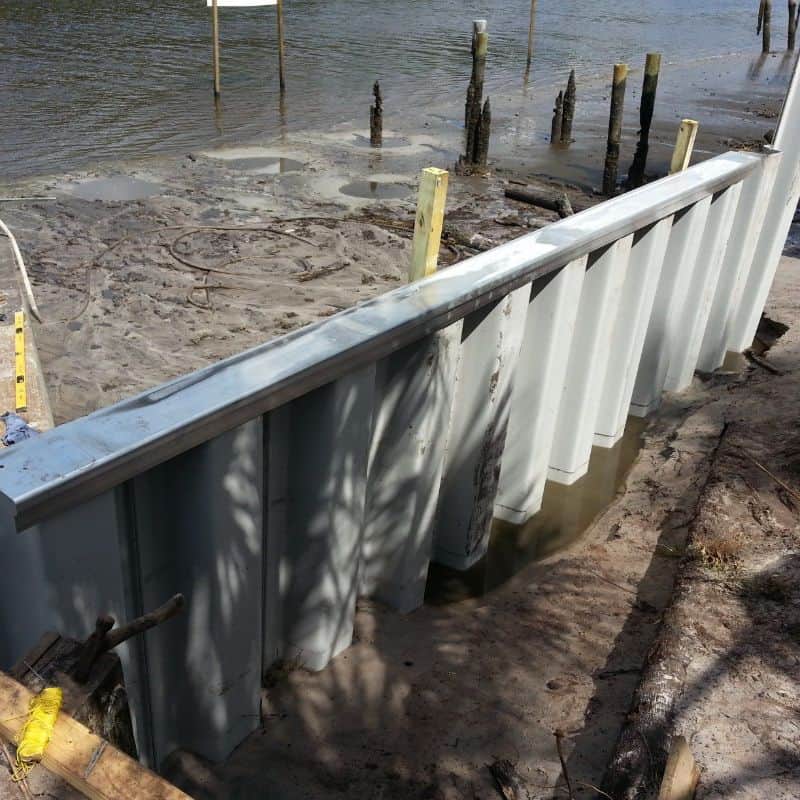 Vinyl sheet pile seawall with steel cap channel newly set in sand, old pilings behind it